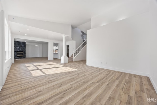 unfurnished living room featuring lofted ceiling, a fireplace, decorative columns, and light hardwood / wood-style flooring