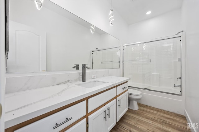 full bathroom featuring bath / shower combo with glass door, hardwood / wood-style floors, vanity, and toilet