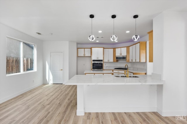 kitchen featuring decorative light fixtures, kitchen peninsula, light hardwood / wood-style floors, and light stone countertops