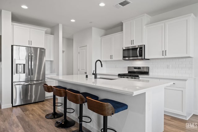 713 Winooski Ct, Bakersfield, CA 93314 - kitchen with appliances with stainless steel finishes, wood finished floors, tasteful backsplash, a center island with sink, and white cabinets