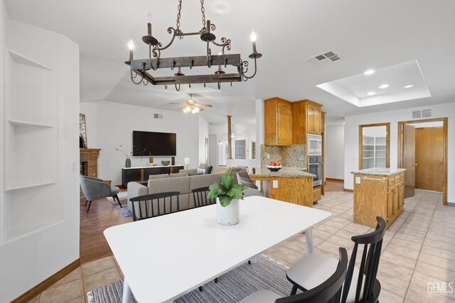 631 Faversham Way, Bakersfield, CA 93311 - dining area featuring a tray ceiling, light tile patterned floors, a ceiling fan, a fireplace, and baseboards