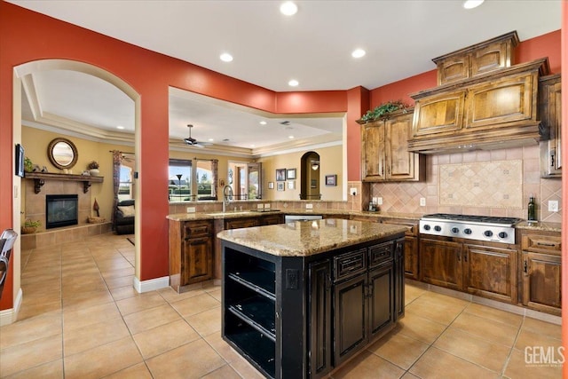 kitchen featuring stainless steel gas cooktop, backsplash, arched walkways, light tile patterned floors, and a tile fireplace