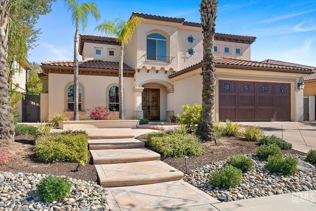 mediterranean / spanish-style house with a tile roof, stucco siding, an attached garage, and concrete driveway