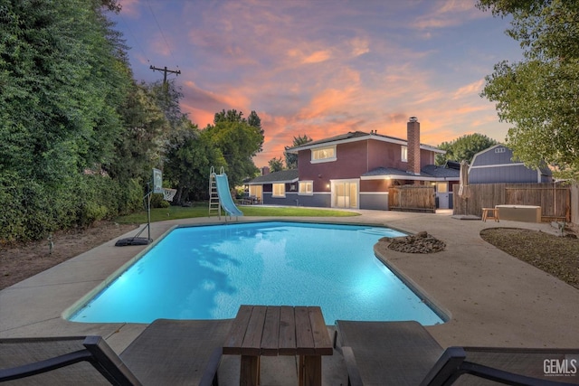 pool at dusk featuring a patio area and a water slide