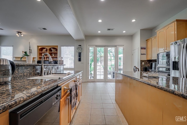 kitchen featuring stainless steel fridge, built in microwave, sink, dark stone countertops, and dishwasher