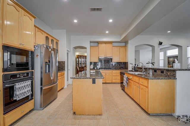 kitchen with dark stone counters, tasteful backsplash, a center island, and black appliances