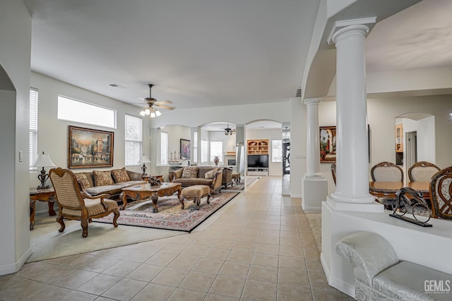 tiled living room featuring ceiling fan, plenty of natural light, and decorative columns