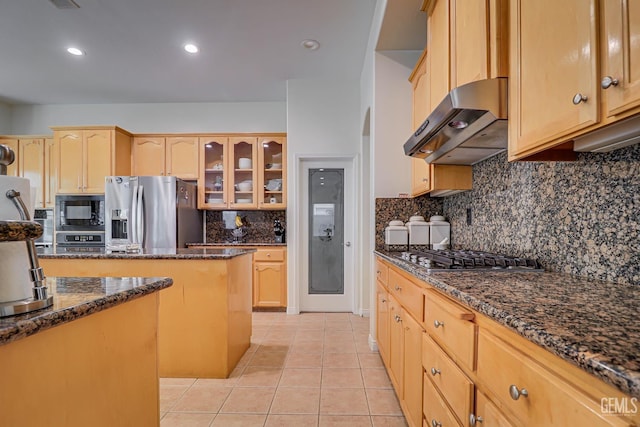 kitchen with exhaust hood, dark stone countertops, light tile patterned floors, appliances with stainless steel finishes, and tasteful backsplash