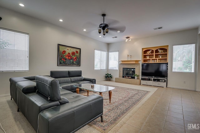 living room with ceiling fan, light tile patterned flooring, built in features, and a tile fireplace