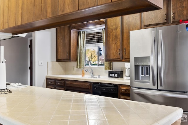 kitchen featuring sink, backsplash, black dishwasher, stainless steel refrigerator with ice dispenser, and tile counters