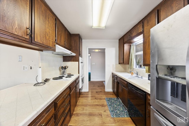 kitchen with tasteful backsplash, sink, tile counters, white appliances, and light hardwood / wood-style flooring