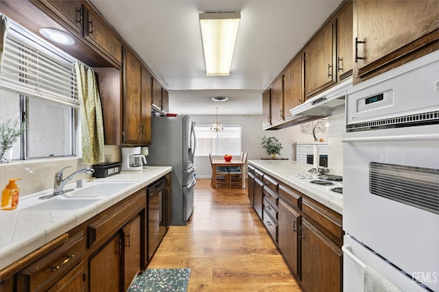 kitchen featuring pendant lighting, sink, white appliances, light hardwood / wood-style floors, and tile countertops