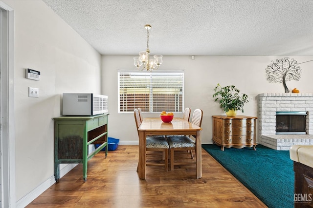 dining room featuring an inviting chandelier, a brick fireplace, hardwood / wood-style flooring, and a textured ceiling