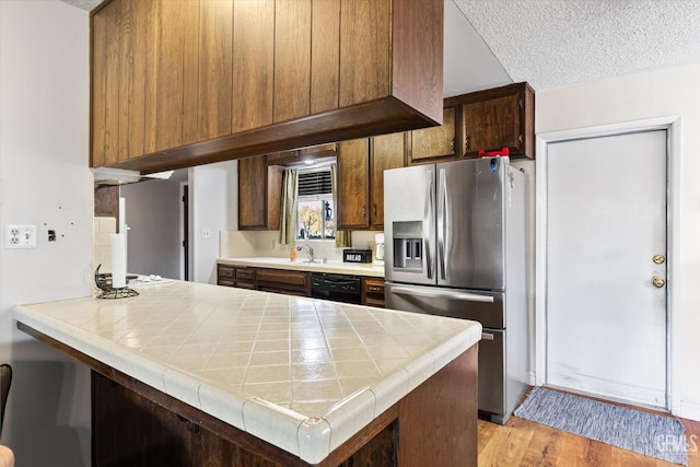 kitchen with dishwasher, stainless steel fridge, tile counters, kitchen peninsula, and light wood-type flooring