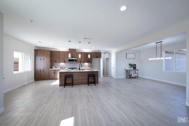 kitchen with hanging light fixtures, tasteful backsplash, light hardwood / wood-style floors, a kitchen island with sink, and a breakfast bar