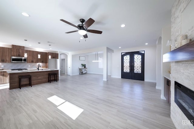 unfurnished living room featuring ceiling fan, a fireplace, french doors, and sink