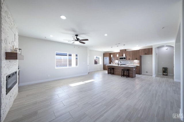 living room with ceiling fan, a stone fireplace, sink, and light hardwood / wood-style flooring