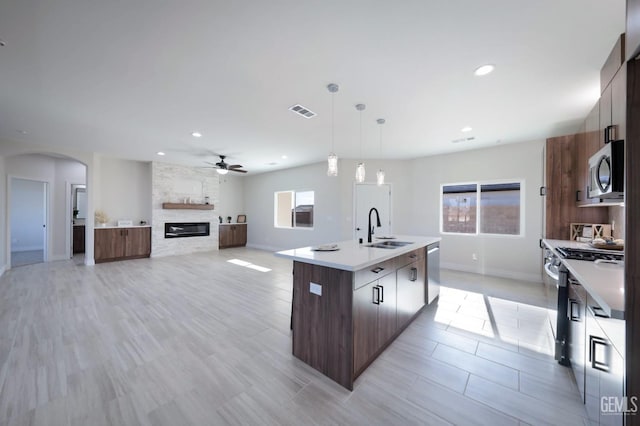 kitchen featuring appliances with stainless steel finishes, dark brown cabinets, a kitchen island with sink, sink, and hanging light fixtures