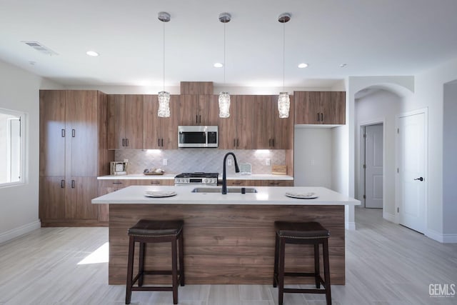 kitchen featuring appliances with stainless steel finishes, backsplash, a kitchen island with sink, sink, and a breakfast bar area