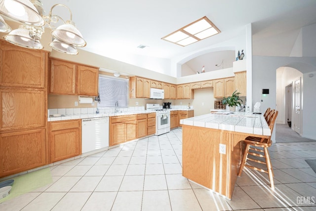 kitchen with a breakfast bar, pendant lighting, high vaulted ceiling, light tile patterned floors, and white appliances