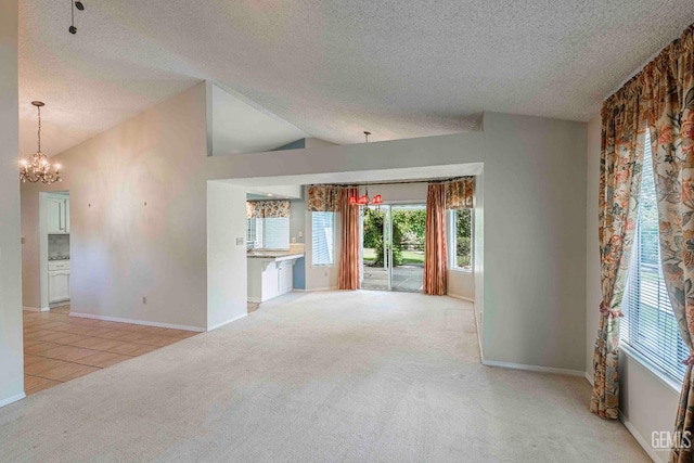 unfurnished living room with a textured ceiling, a chandelier, carpet flooring, lofted ceiling, and baseboards