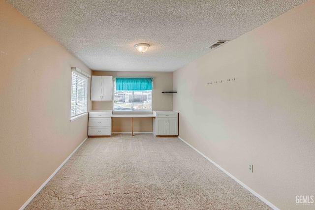 unfurnished bedroom with built in desk, visible vents, light colored carpet, and baseboards