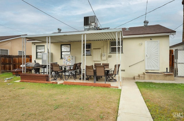 rear view of property with a yard, stucco siding, a shingled roof, central AC, and fence