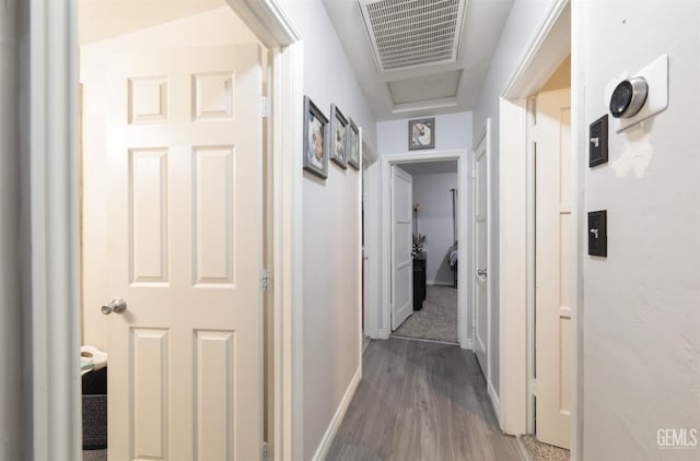 corridor featuring attic access, dark wood-style flooring, visible vents, and baseboards