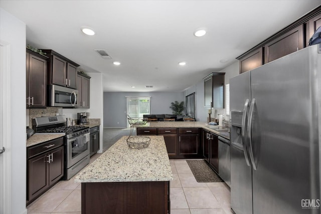 kitchen with stainless steel appliances, a kitchen island, dark brown cabinets, light stone counters, and light tile patterned flooring