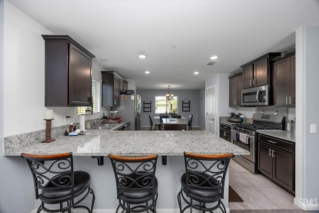 kitchen featuring appliances with stainless steel finishes, a peninsula, dark brown cabinets, a kitchen bar, and a chandelier
