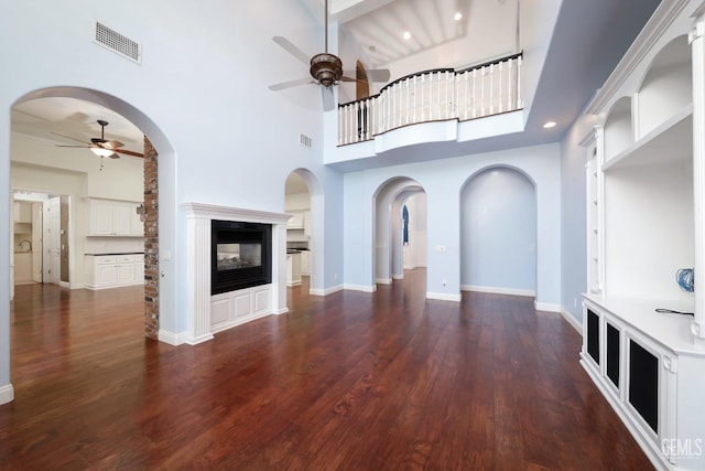 unfurnished living room featuring a multi sided fireplace, ceiling fan, dark hardwood / wood-style flooring, and a high ceiling