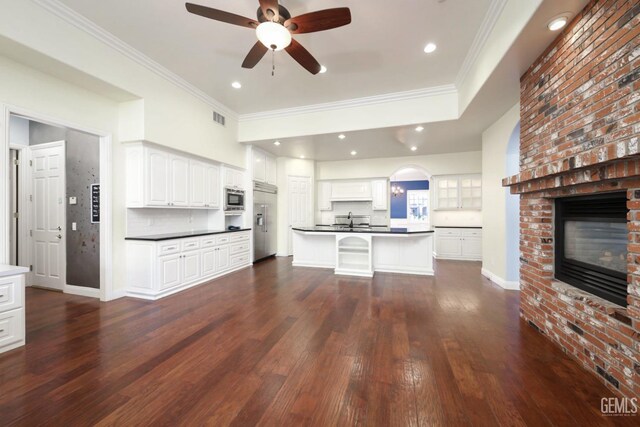 kitchen featuring backsplash, white cabinets, crown molding, a brick fireplace, and built in appliances