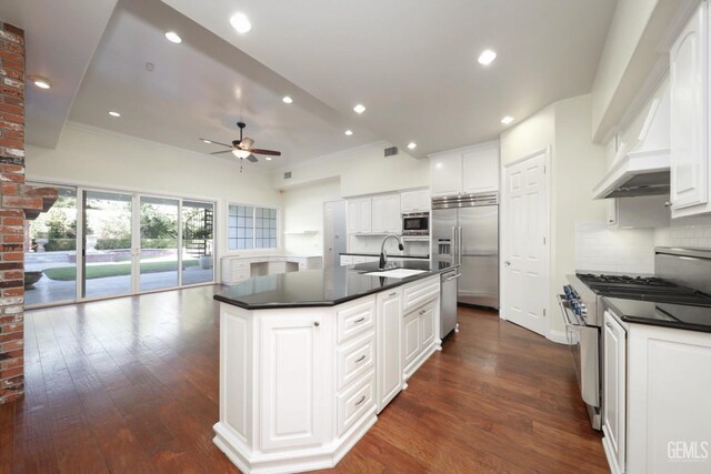 kitchen with built in appliances, ceiling fan, white cabinets, and a kitchen island with sink