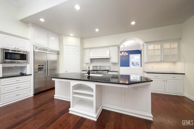 kitchen featuring backsplash, built in appliances, a center island with sink, and white cabinets