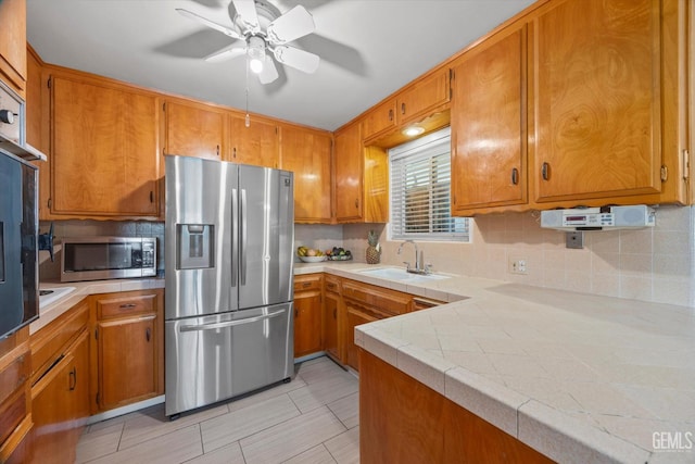 4501 Chadbourn St, Bakersfield, CA 93307 - kitchen featuring appliances with stainless steel finishes, brown cabinetry, backsplash, ceiling fan, and light countertops