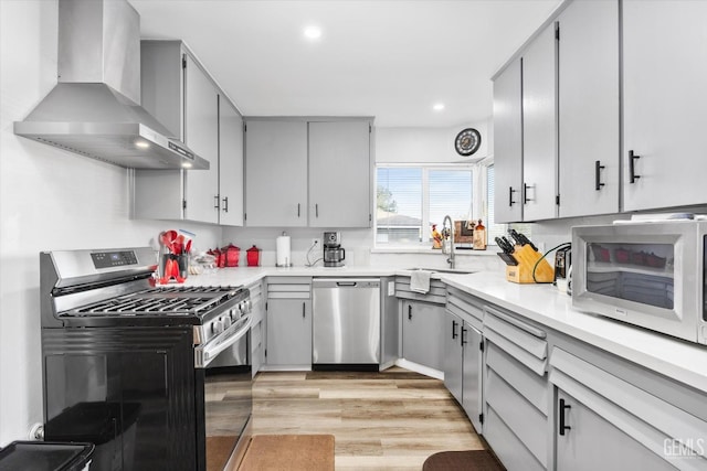 kitchen featuring wall chimney range hood, sink, gray cabinetry, stainless steel appliances, and light wood-type flooring