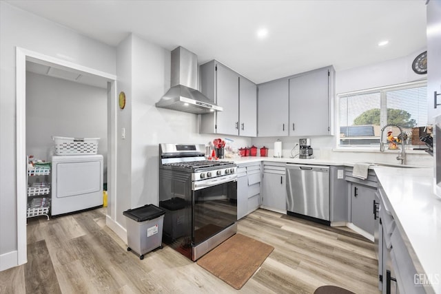 kitchen featuring wall chimney range hood, sink, appliances with stainless steel finishes, washer / clothes dryer, and light wood-type flooring