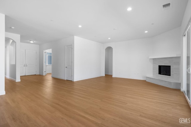 8708 Tamburlane Ct, Bakersfield, CA 93314 - unfurnished living room featuring arched walkways, light wood finished floors, a fireplace with raised hearth, and recessed lighting