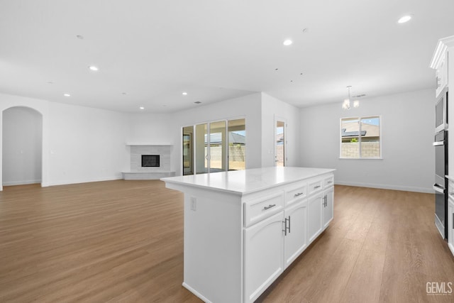 8708 Tamburlane Ct, Bakersfield, CA 93314 - kitchen featuring a glass covered fireplace, a kitchen island, recessed lighting, arched walkways, and light wood-style floors