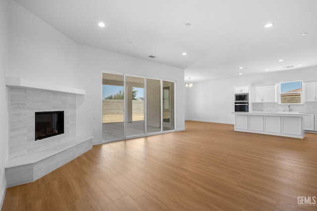 8708 Tamburlane Ct, Bakersfield, CA 93314 - unfurnished living room featuring a fireplace with raised hearth, light wood-type flooring, and recessed lighting