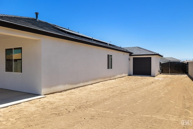 8708 Tamburlane Ct, Bakersfield, CA 93314 - back of house with stucco siding, dirt driveway, a garage, and solar panels