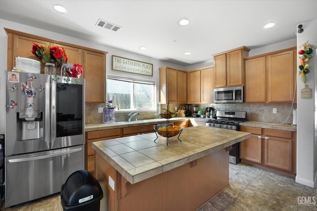 kitchen featuring appliances with stainless steel finishes, tile countertops, a center island, and backsplash