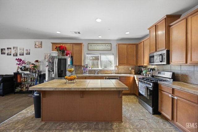 kitchen featuring tile countertops, decorative backsplash, a kitchen island, a kitchen bar, and appliances with stainless steel finishes