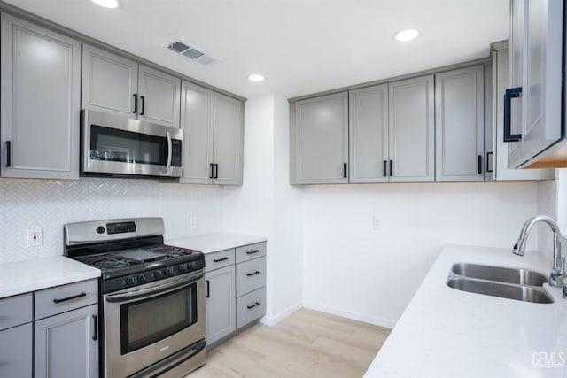 kitchen featuring appliances with stainless steel finishes, gray cabinets, sink, and light wood-type flooring