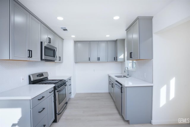 kitchen with stainless steel appliances, sink, light hardwood / wood-style flooring, and gray cabinets