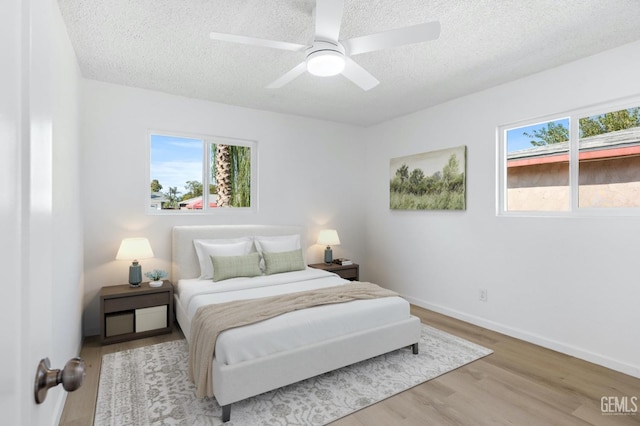 bedroom with a textured ceiling, ceiling fan, and light hardwood / wood-style flooring