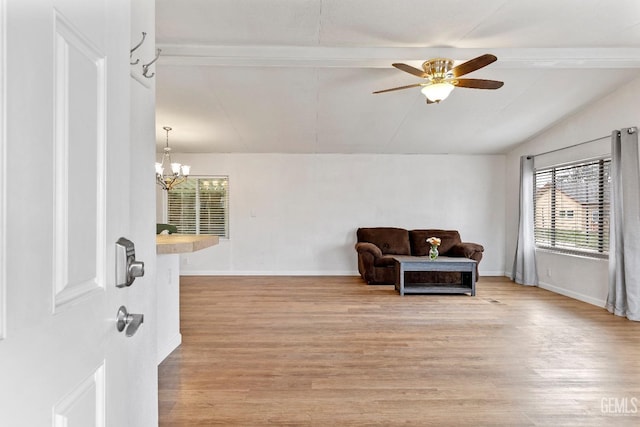 living area featuring ceiling fan with notable chandelier, light wood-type flooring, and vaulted ceiling