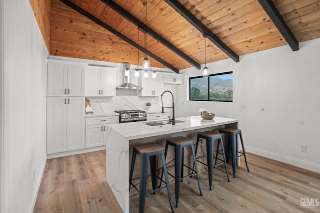 24501 Pueblo Ct, Tehachapi, CA 93561 - kitchen featuring wall chimney range hood, a wood ceiling with exposed beams, stainless steel range with gas cooktop, light wood-style floors, and white cabinetry