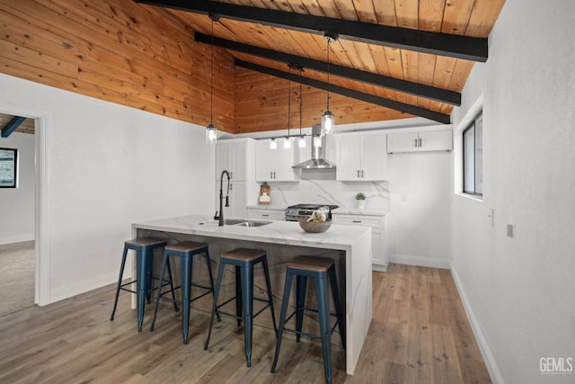 24501 Pueblo Ct, Tehachapi, CA 93561 - kitchen with wood ceiling, white cabinetry, a center island with sink, a breakfast bar area, and wall chimney range hood