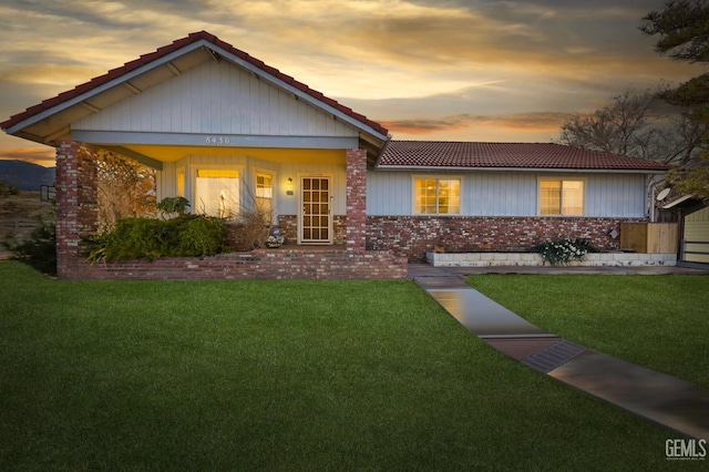 view of front of property with brick siding, a tiled roof, and a front lawn